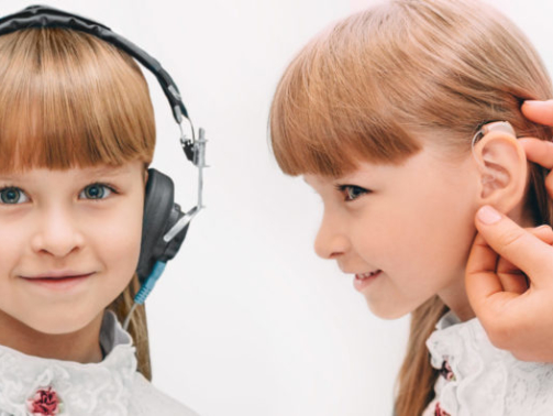 Set, little girl wearing headphones having a hearing test and after hearing test, doctor places a hearing aid in her ear.