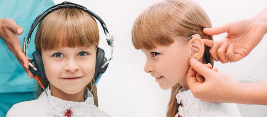 Set, little girl wearing headphones having a hearing test and after hearing test, doctor places a hearing aid in her ear.